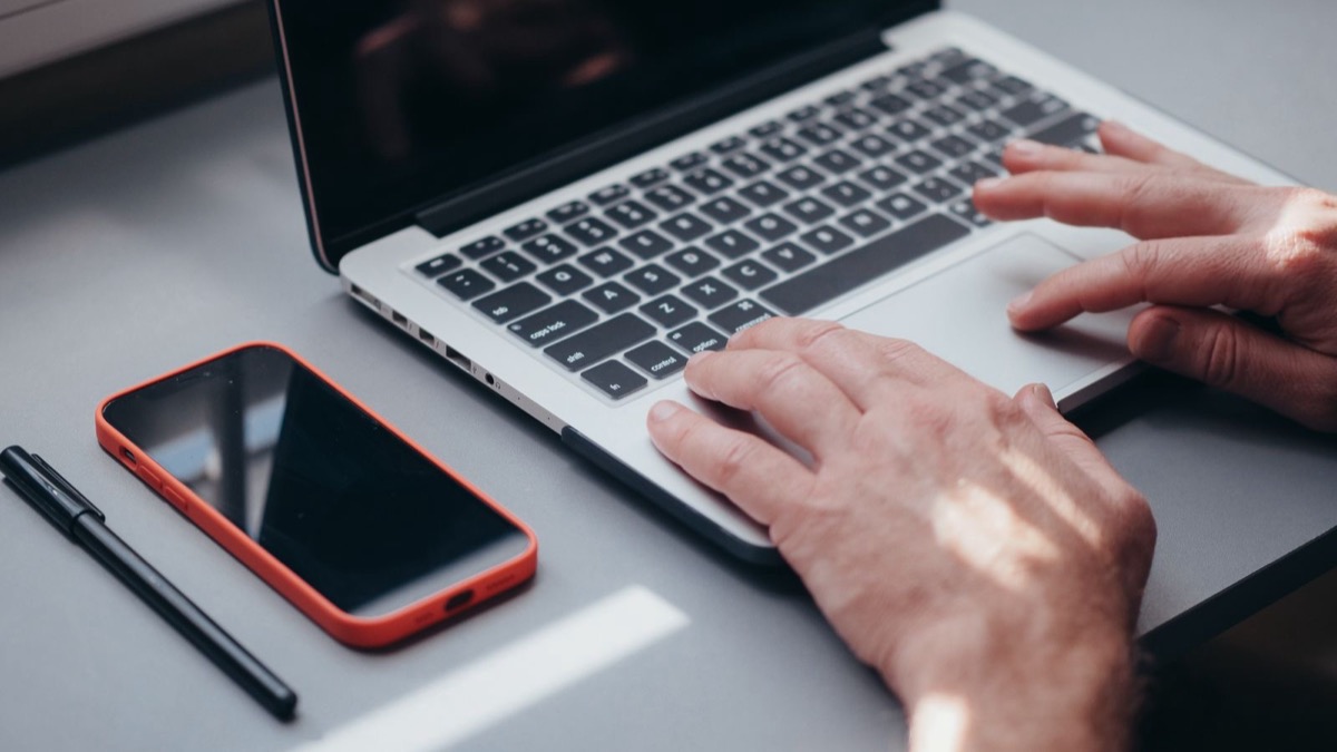 Hands on a laptop keyboard beside a phone and a pen