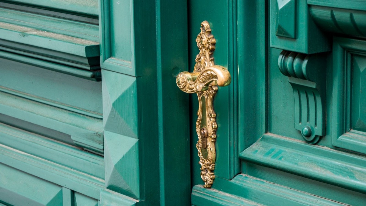 A green panelled door with an ornate brass handle