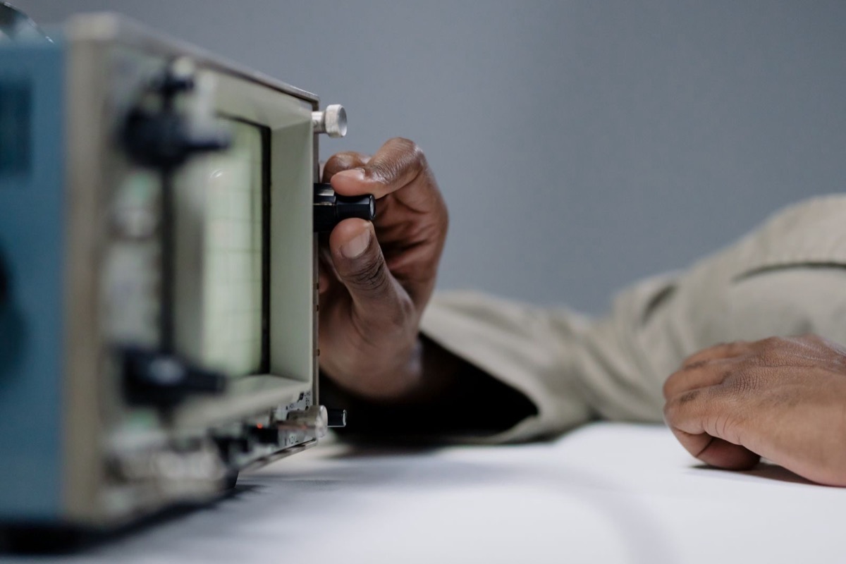 A hand turning the dial of an oscilloscope on a bench
