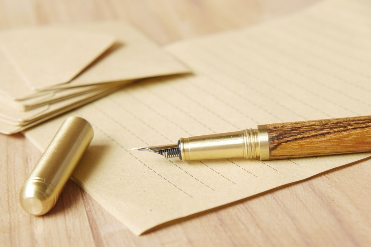 A fountain pen and its cap on lined paper beside kraft envelopes
