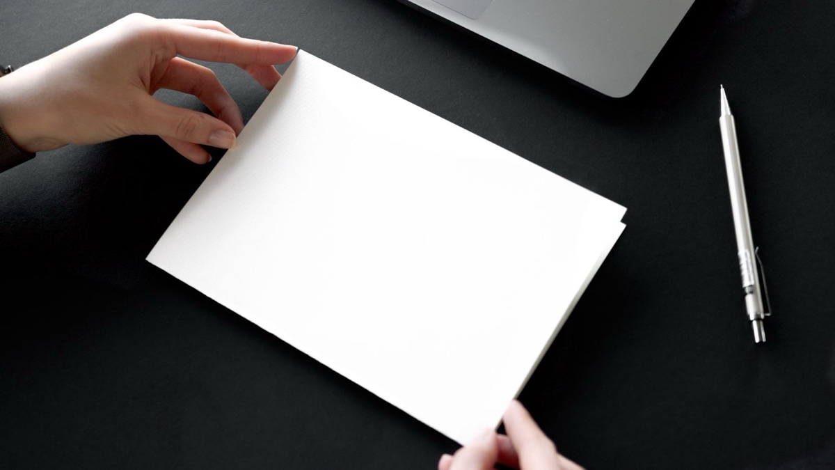 Hands holding a blank sheet beside a pencil and a laptop