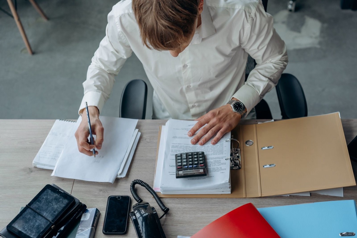 A man working through papers and an open binder with a calculator at a desk