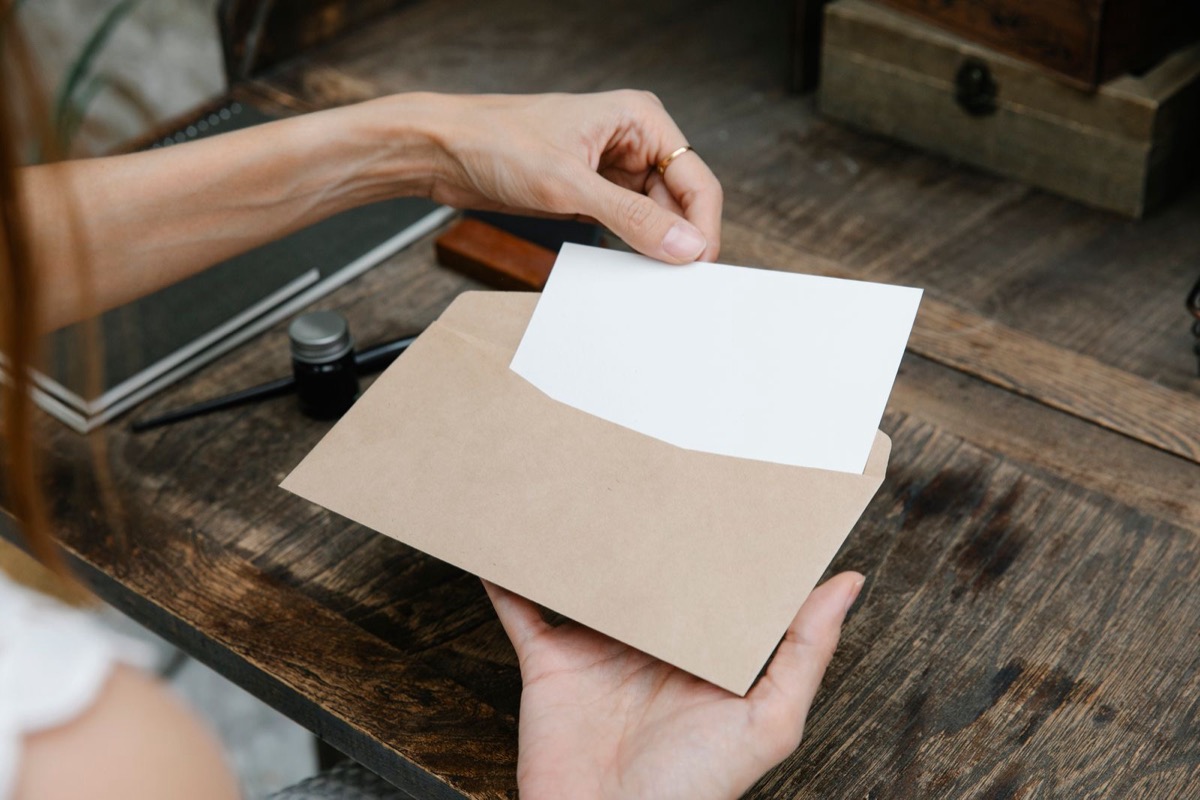 Hands slipping a blank card into a kraft envelope at a wooden desk